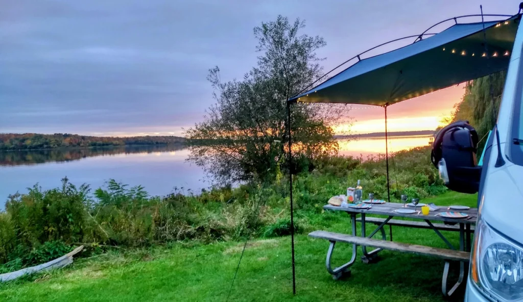 A photo of van life family eating outside their van in scenic area of a lake.