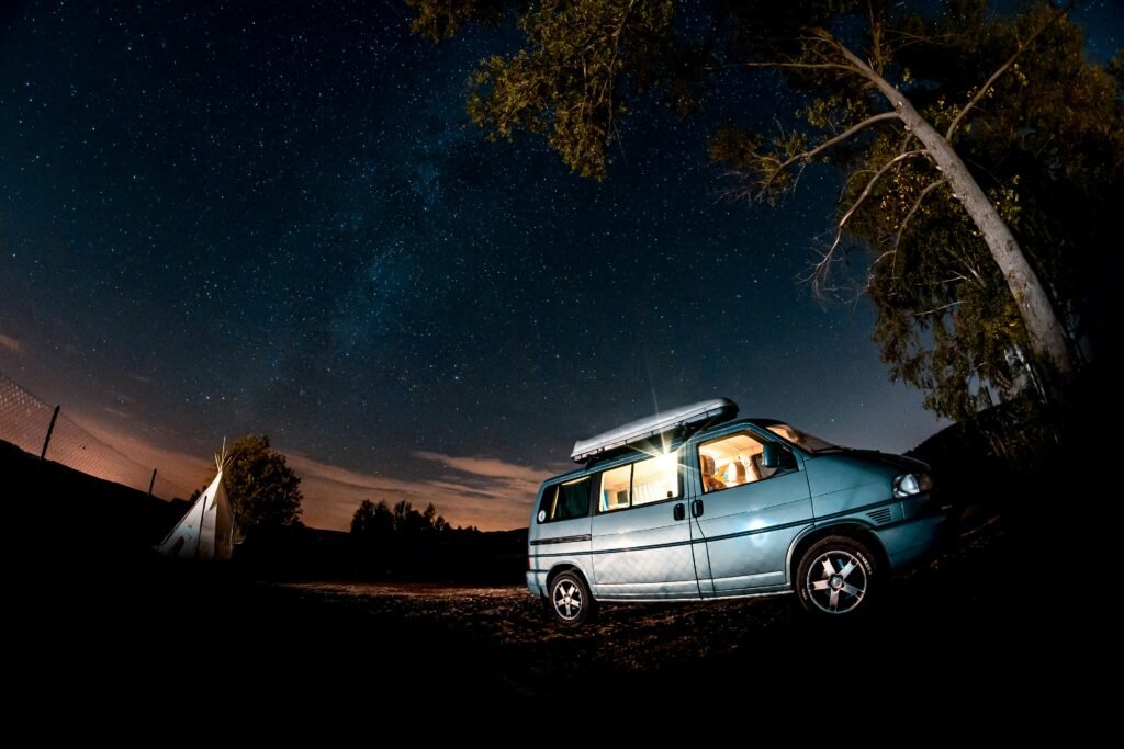 A camper van parked in a dispersed land in nature at night.