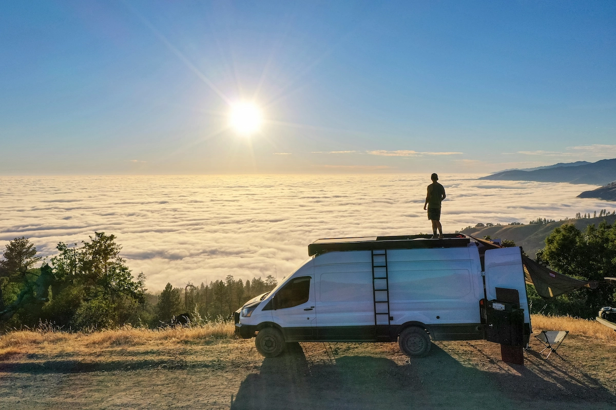 Camper van parked in the mountains with a man standing on top, symbolizing van life freedom