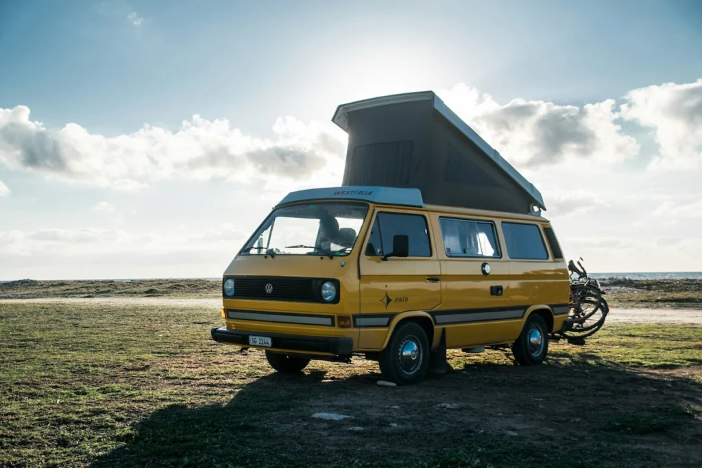 An image of a camper van parked on an open field in a bright sunny weather