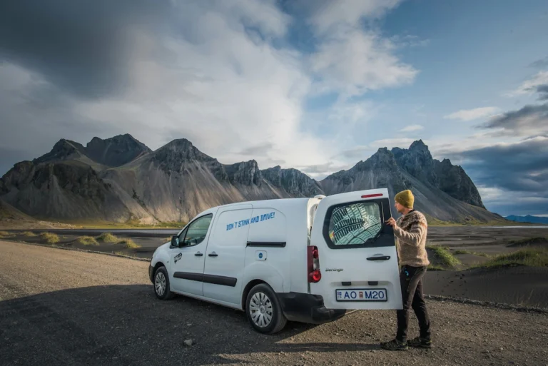 A photo of a low-roof cargo van converted to a camper van parked in a scenic mountain landscape.