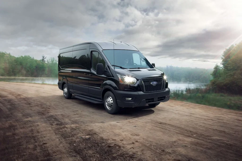 A photo of a Ford Transit high-roof cargo van driving through a road.